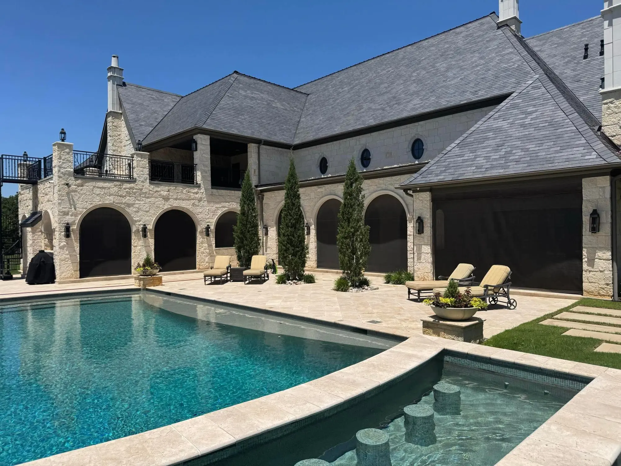 An EX Design Group poolside project with motorized screens at stone-arched patio openings.