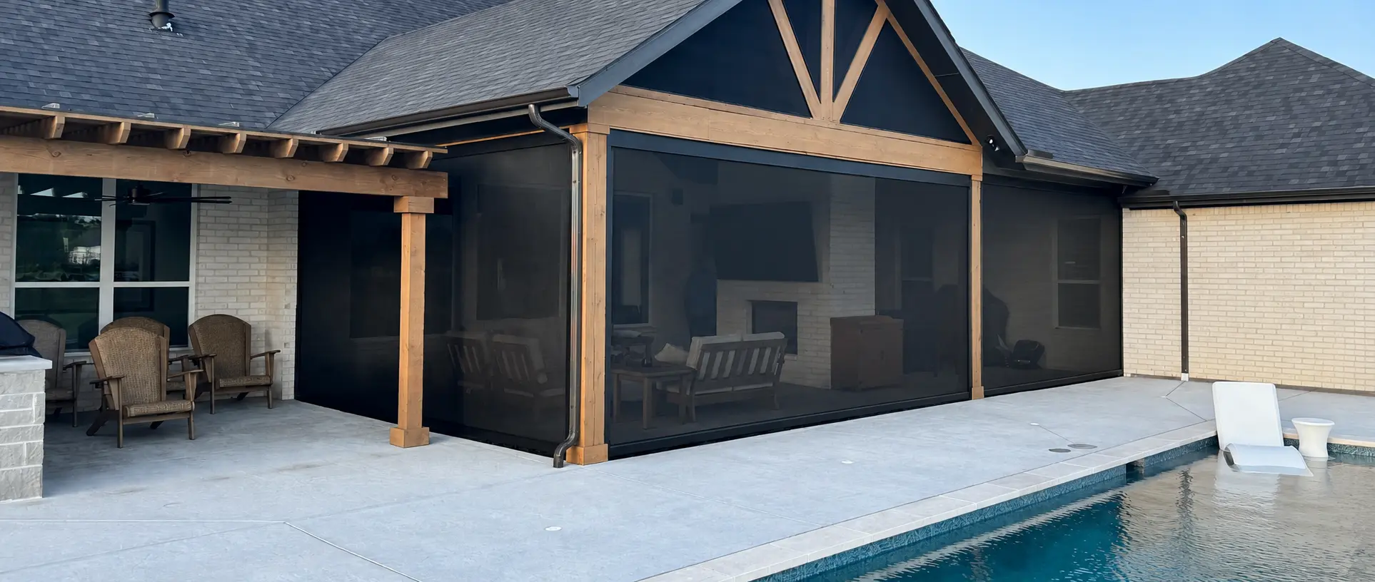 Fully lowered motorized screens around a timber-framed patio beside a swimming pool.